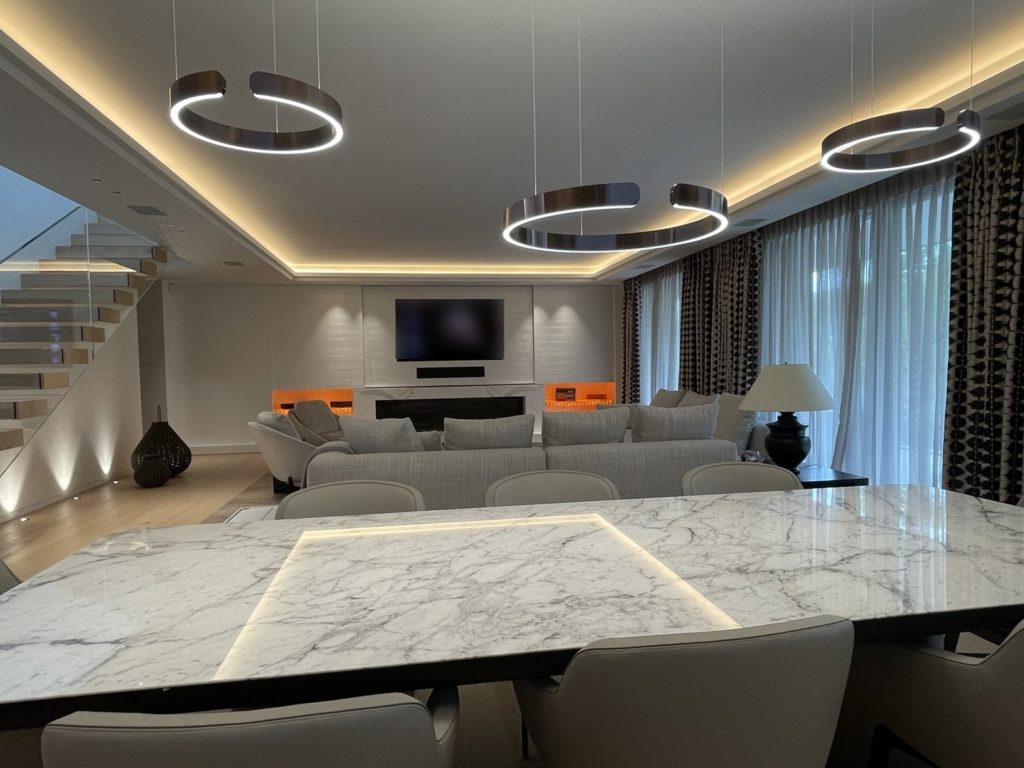 Séjour d'un appartement à Genève : suspensions circulaires, corniche lumineuse et table en marbre rétroéclairée