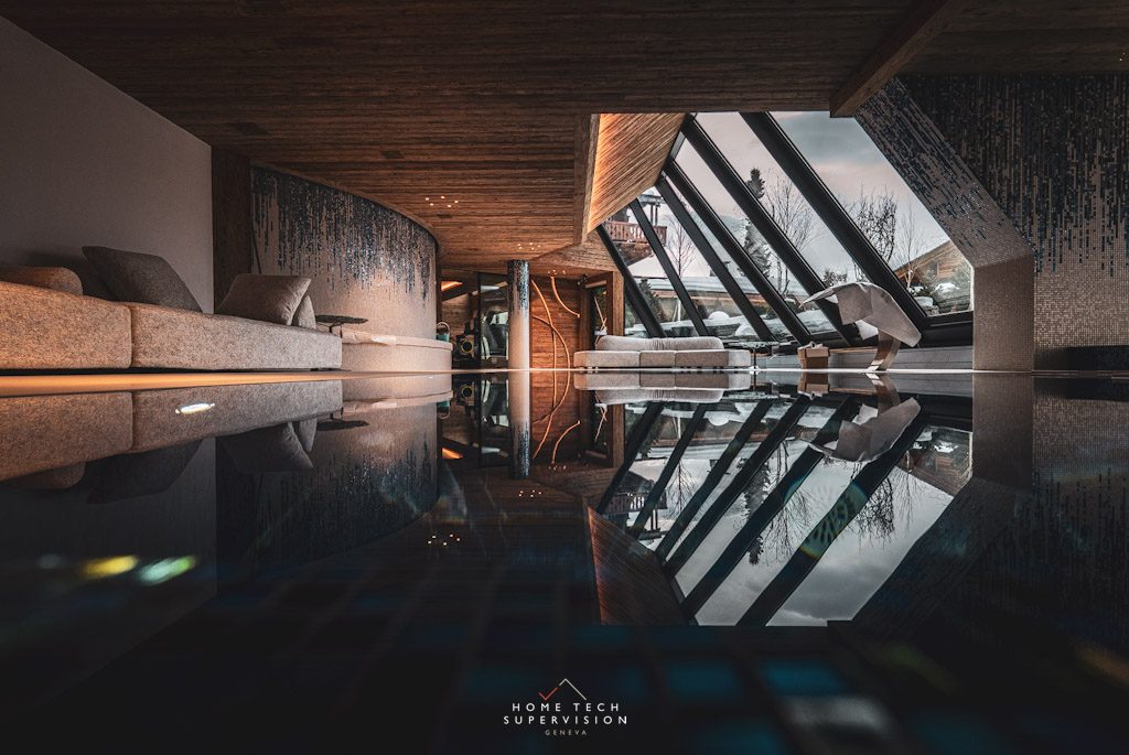 Reflet du salon et de la baie vitrée dans la piscine d'un chalet en Valais