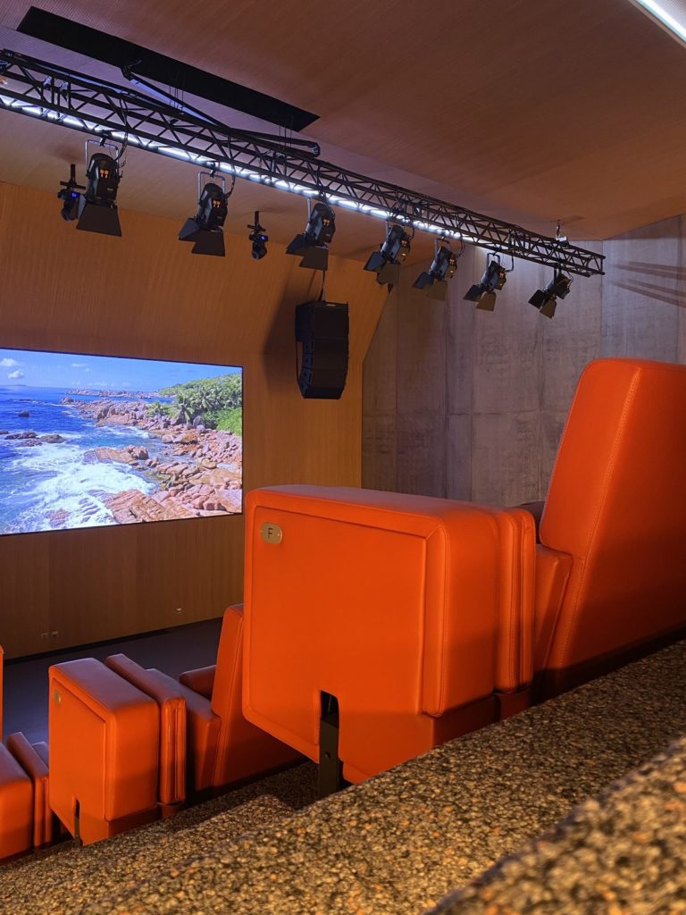 Fauteuils orange au premier plan, mur LED et pont de projecteurs de scène