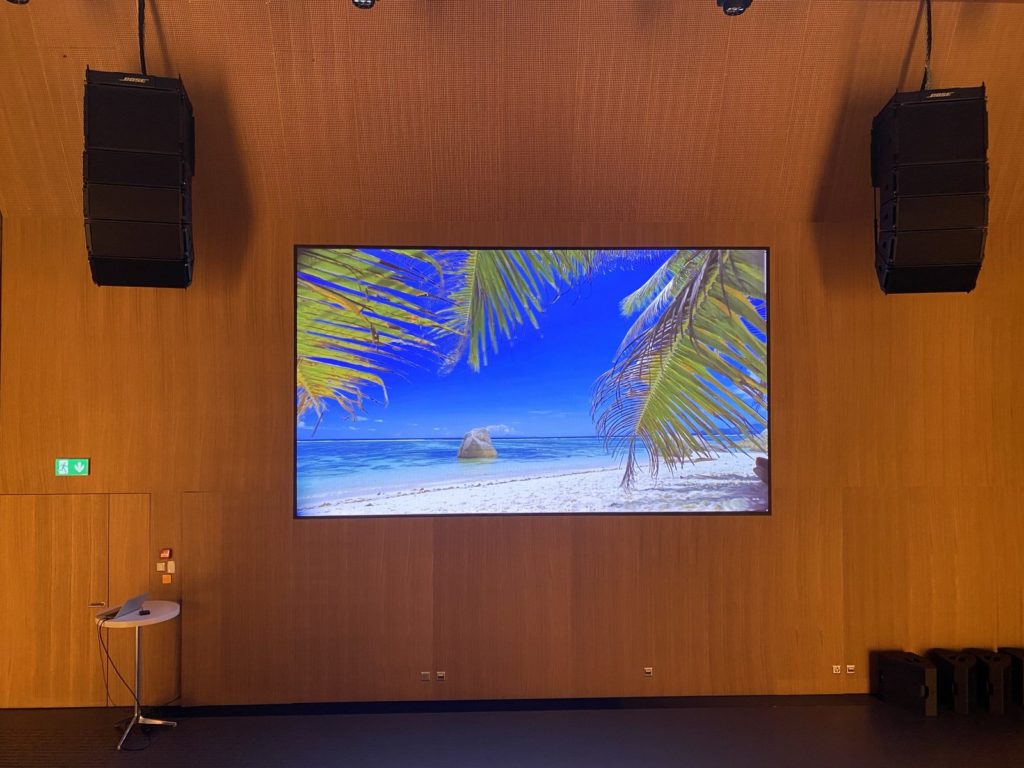 Mur LED encastré dans le parement bois de l’auditorium, encadré de deux line arrays Bose