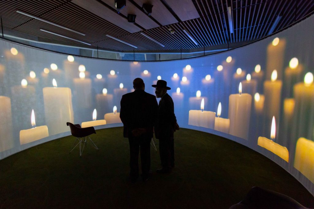 Alcôve avec projection d’un champ de bougies et deux visiteurs en silhouette