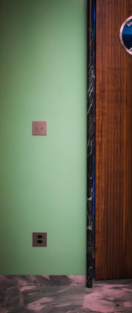 Interrupteur et prise bronze sur mur vert, porte en noyer