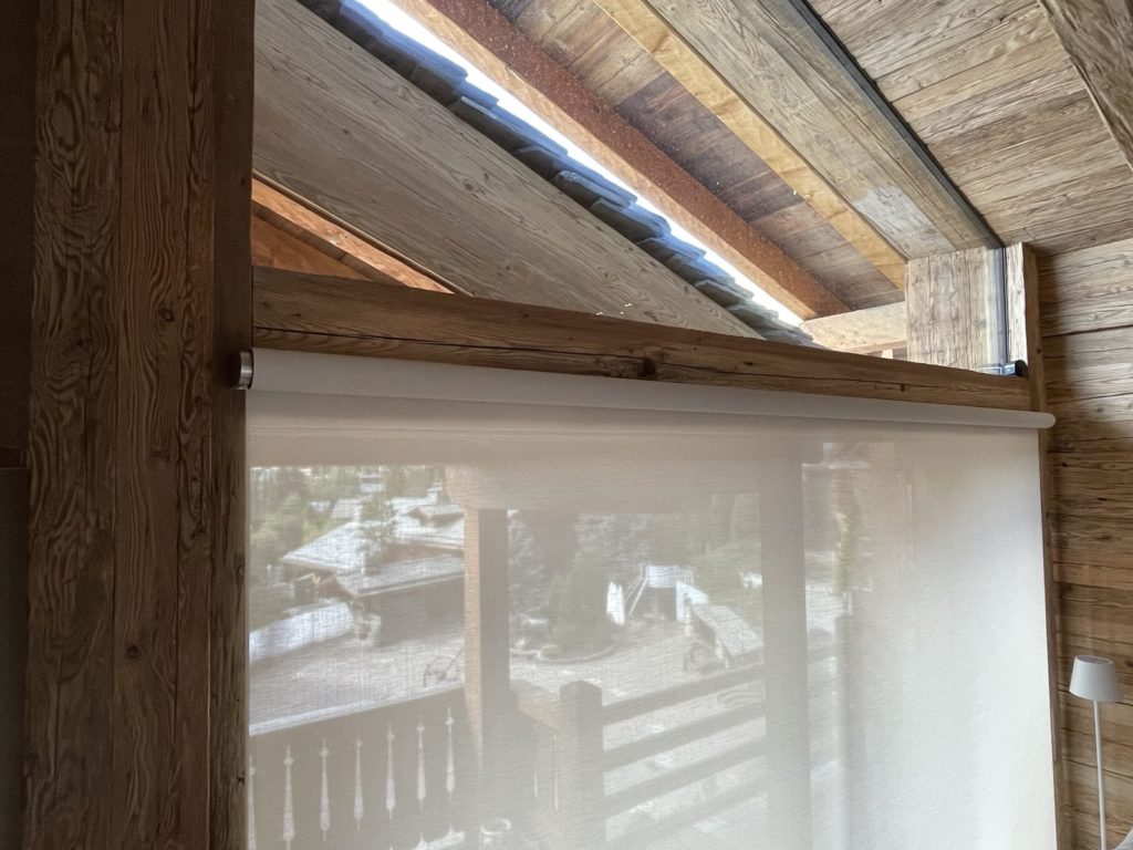 Tube de store Lutron fixé sous une poutre en vieux bois, sans câble apparent