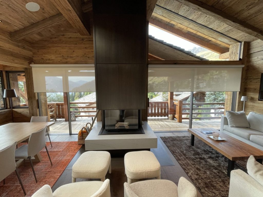 Stores toile Lutron arrêtés à mi-hauteur devant les baies d’un salon de chalet en vieux bois